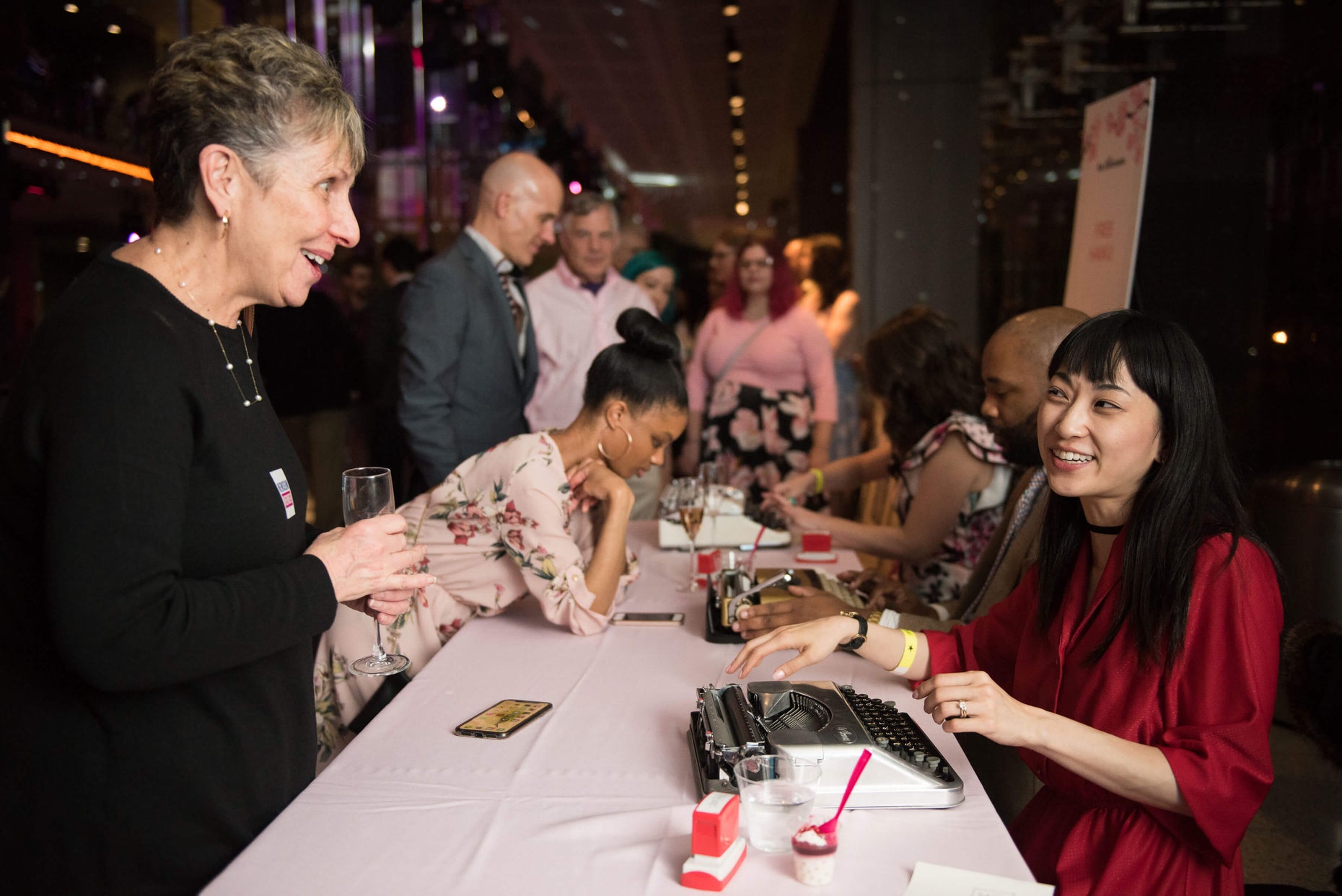 People engaging at an event table with typewriters and drinks.