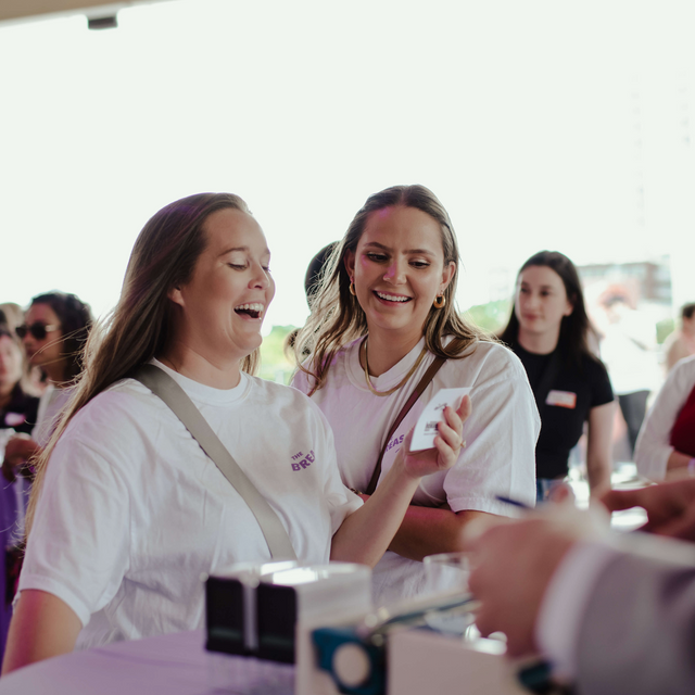 Two women in white t-shirts laughing and interacting at an event.